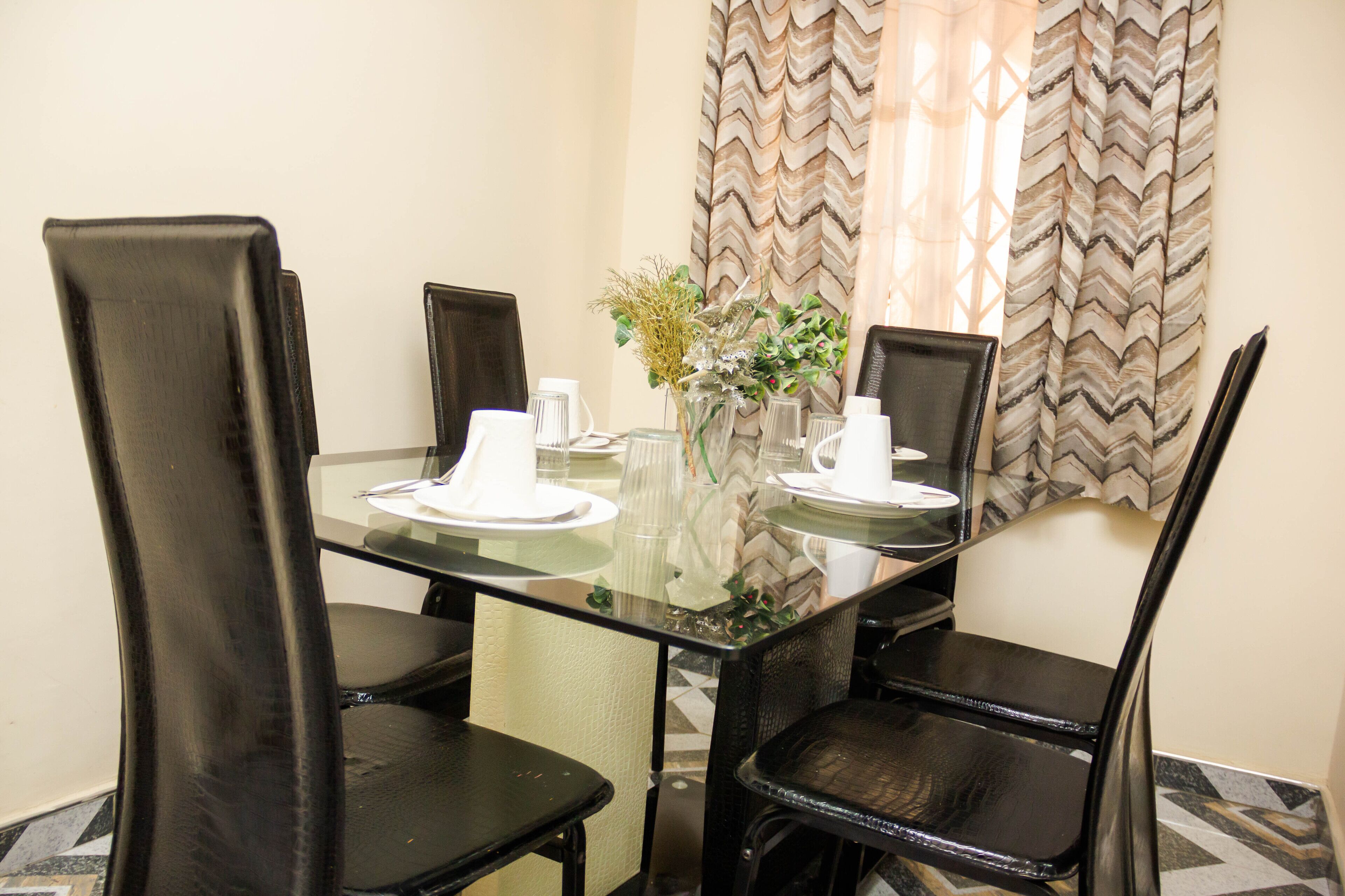 A dining table with four chairs, a vase with flowers, and a glass top.