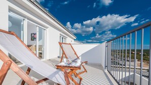 A balcony with two wooden lounge chairs, a small table with cups and a jar of candies, and a glass door leading to an interior room. - Dalmacija III in Suko an (Sukosan)