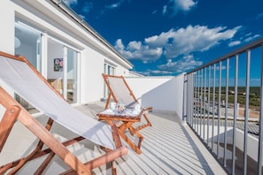 Ein Balkon mit zwei Holzliegen, einem kleinen Tisch mit Tassen und einer Süßschale sowie einer Glastür zu einem Innenraum.