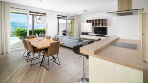 Een moderne woonkamer met een eethoek, een keuken en een schuifdeur naar een balkon met uitzicht op zee.