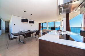 A modern kitchen with a large island, dining area with chairs, and a view of the sea. - Adria II in Primo ten (Primosten)