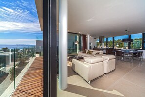 Una sala de estar moderna con un sofá grande, un comedor con una mesa y sillas, y vista al océano.