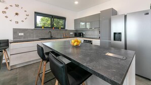 A modern kitchen with a central island, stainless steel appliances, and a clock on the wall. - Althea in Ru i i With 4 Bedrooms and 4 Bathrooms (Sveta Nedelja)