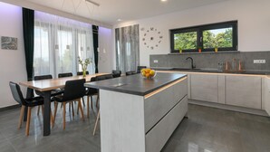 A modern kitchen with a central island, dining area with chairs, and a large window with a view of trees. - Althea in Ru i i With 4 Bedrooms and 4 Bathrooms (Sveta Nedelja)
