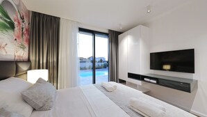 Camera d'albergo moderna con un letto grande, una TV a schermo piatto, una scrivania e vista su una piscina.
