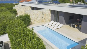 Una piscina sul tetto con lettini, circondata da mura in pietra e vegetazione, con vista su una zona costiera.