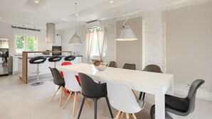 Una cocina moderna con armarios blancos, una isla central y un área de comedor con una mesa blanca y sillas blancas y negras.