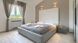 Un dormitorio moderno con una cama grande, mesitas de noche y un ventanal con cortinas.