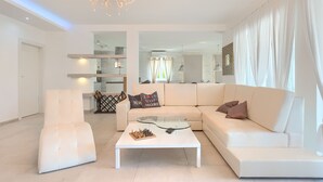Una sala de estar moderna con un sofá blanco, una mesa de centro de cristal y un sillón blanco.