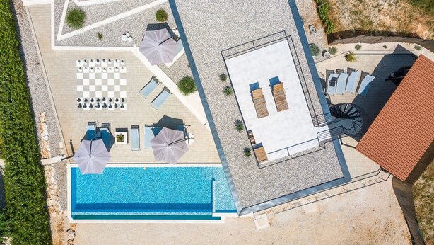 Vista aérea de un complejo turístico con piscina, tumbonas, una zona de estar a cuadros y un área de estar cubierta.