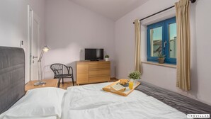 Ett sovrum med en säng, ett nattduksbord, en lampa, en tv, en byrå och ett fönster med gardiner.