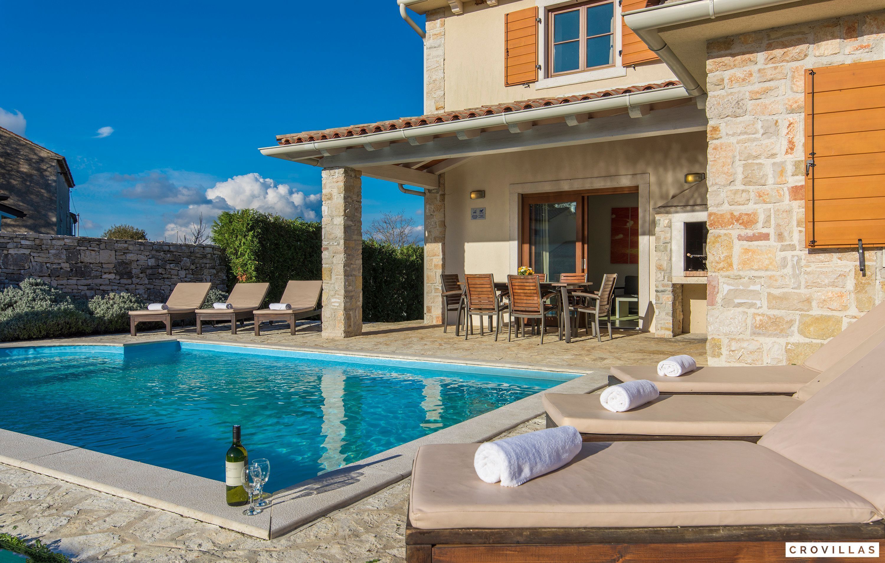 A poolside area with lounge chairs, a table, and a bottle of wine.