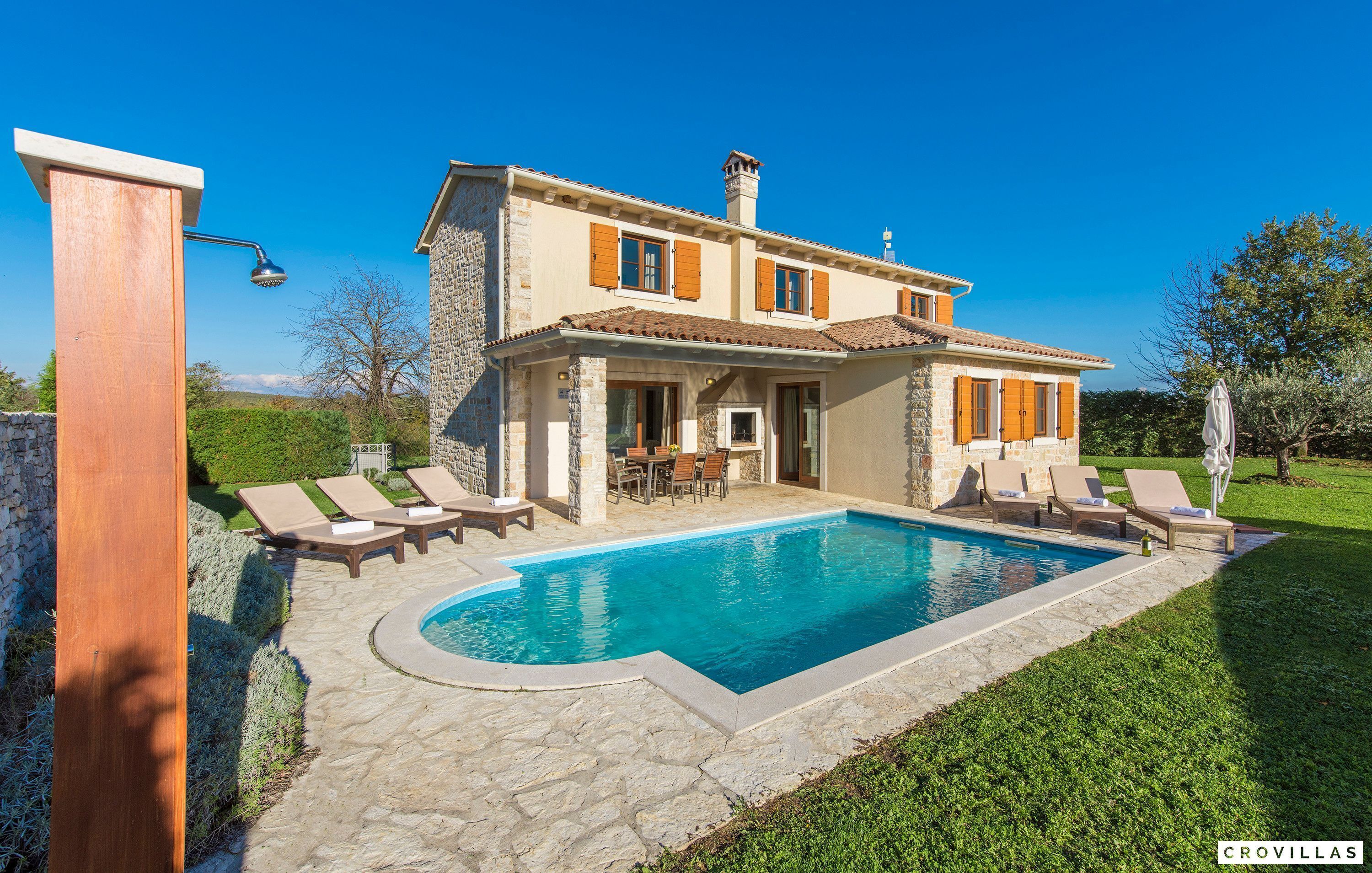 A two-story house with a swimming pool, stone exterior, and wooden shutters.