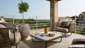 A balcony with wicker furniture, a table with books and fruit, and a view of greenery and buildings. - Zoe in Ladi i With 4 Bedrooms and 4 Bathrooms (Kanfanar)