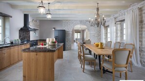 A spacious kitchen with a central island, wooden dining table, and chairs, stone walls, and a chandelier. - Zoe in Ladi i With 4 Bedrooms and 4 Bathrooms (Kanfanar)