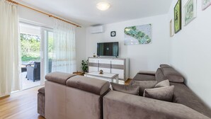 Un salon comprenant un canapé, un téléviseur posé sur un meuble en bois et une porte-fenêtre coulissante donnant sur un espace extérieur.
