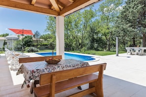 Ein Außenbereich mit Terrasse, Pool, Holzmöbeln und einem roten Sonnenschirm.