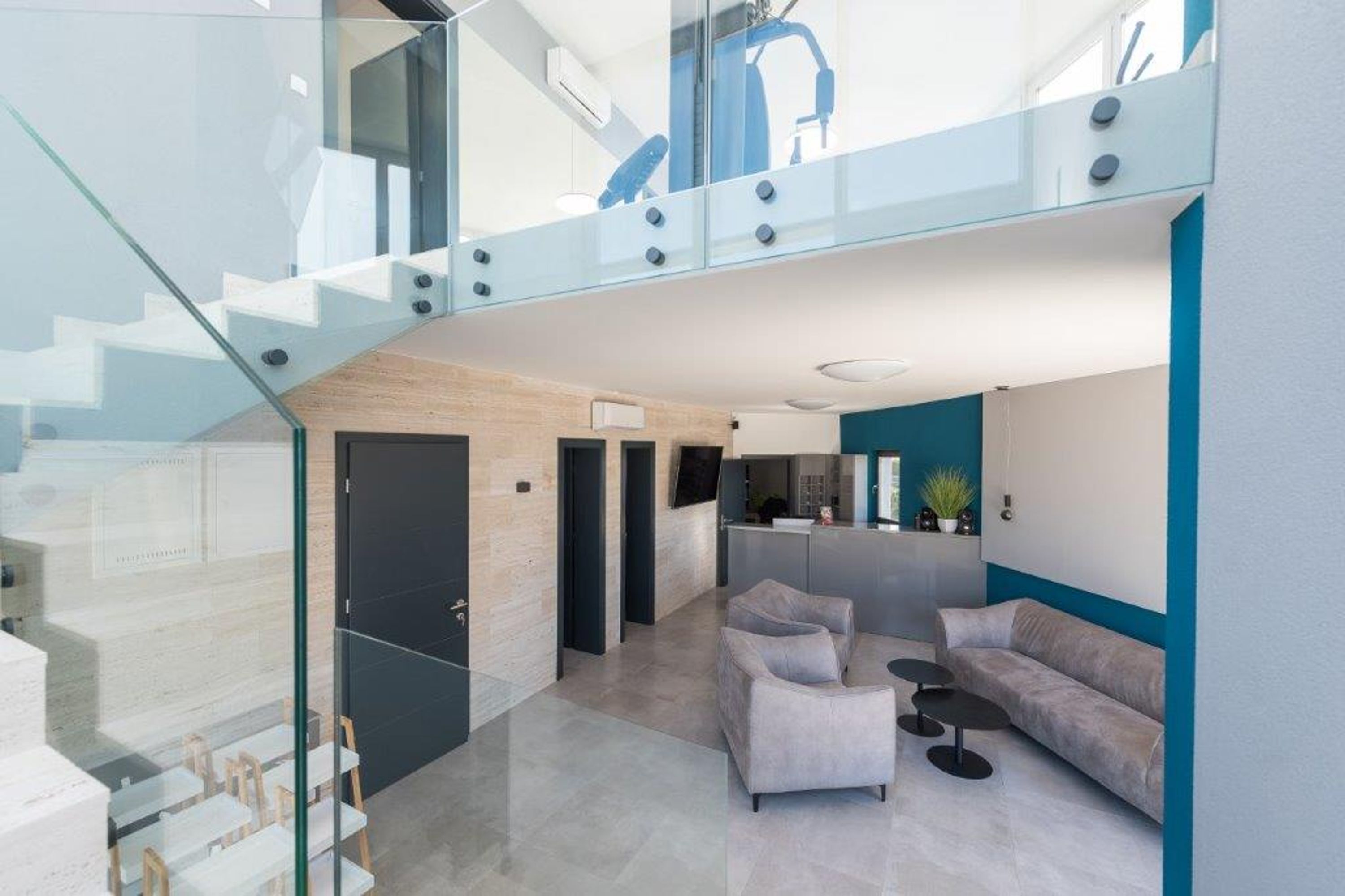 Un interior moderno con una escalera, una sala de estar con sofá y sillones, y una zona de cocina.