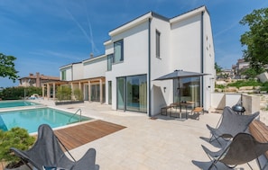 Ein modernes, zweistöckiges Haus mit Swimmingpool, Sitzgelegenheiten im Freien und einer Terrassenanlage.