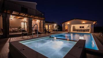 Una piscina con hidromasaje, mobiliario exterior y un patio cubierto.