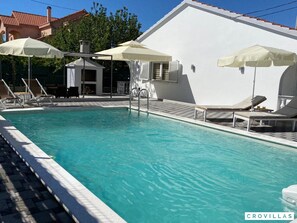 Ein Swimmingpool mit Liegestühlen und Sonnenschirmen, umgeben von einem weißen Gebäude mit einem Ziegeldach.