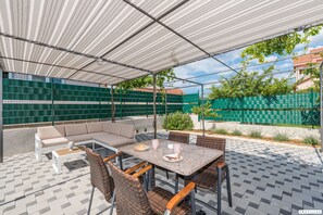 Eine Außenpatio mit überdachter Sitzgelegenheit, einem Tisch mit Stühlen und Blick auf die umliegende Natur und Gebäude.