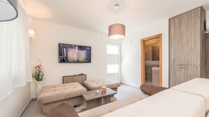 Una sala de estar moderna con un sofá, un reposapiés y una mesa de centro. Hay un televisor montado en la pared y una puerta que da a un baño.