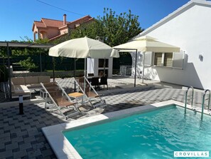 Ein Poolbereich mit Liegestühlen, Sonnenschirmen und einer gefliesten Terrasse.