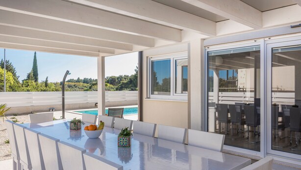 An outdoor dining area with a pool view, white furniture, and a glass door leading to a balcony. - Oliva in Premantura With 6 Bedrooms and 6 Bathrooms (Medulin)