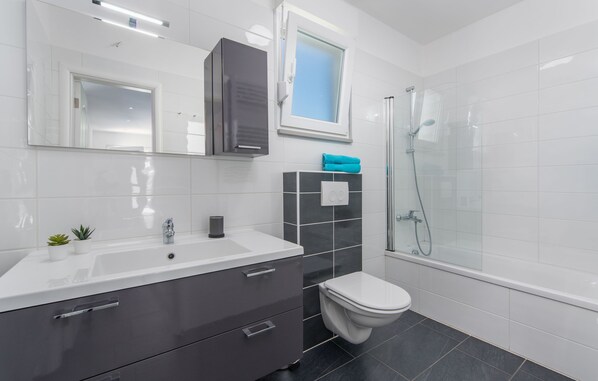 Een moderne badkamer met een wit wastafelmeubel, donkergrijze kastjes, een witte toilet en een douche met glazen wanden.