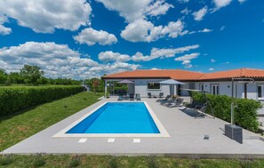 Een modern huis met een zwembad, terras en een verzorgde tuin.