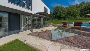 Ein modernes Haus mit Terrasse, Sitzgelegenheiten im Freien und einem Swimmingpool.