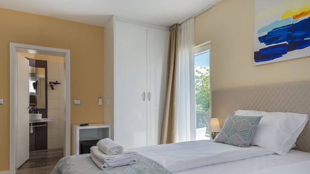 A hotel room with a bed, a nightstand, a bathroom visible through an open door, and a painting on the wall. - Loki in Vi Inada With 4 Bedrooms and 4 Bathrooms (Vizinada)