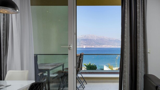 A balcony with a view of the sea and mountains, a dining table, chairs, and a lamp. - Acadia D in Slatine With 6 Bedrooms and 3 Bathrooms (Split)