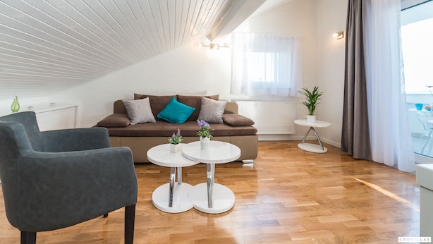 Een moderne woonkamer met een bruine bank, twee witte ronde tafels en een grijze fauteuil.