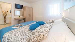 Een slaapkamer met een bed, een televisie erboven, een houten kledingkast en een raam met gordijnen.