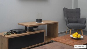 Ein modernes Wohnzimmer mit einer Holzeinrichtungsanlage, einem flachbildfernseher an der Wand, einem grauen Sessel und einem Couchtisch mit einer Zitronenschale.