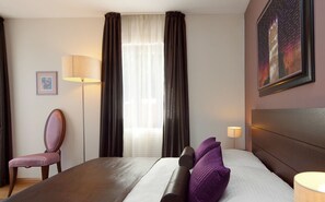 Quarto de hotel com cama, poltrona, abajur e um quadro na parede.