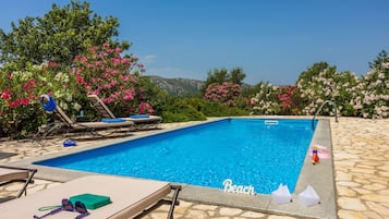 A swimming pool with lounge chairs, a stone tiled deck, and pink flowering bushes.