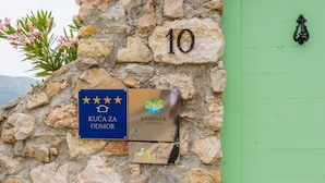 Eine Steinsäule mit der Zahl '10' und drei Schildern mit den Aufschriften 'Kuća odmor', 'Kvarner Family Quality' und 'Haustiere erlaubt'.