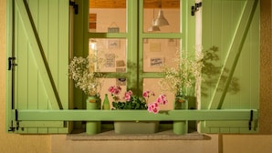 Ein grünes Fenster mit Fensterläden, einer Hängelampe und einem Blumenbrett mit Topfpflanzen und gerahmten Notizen.