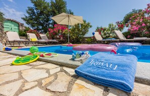 Un espace aménagé au bord de la piscine, avec des chaises longues, une piscine et une serviette sur laquelle est inscrit le mot « TRIBAL ».