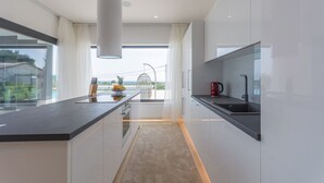 Een moderne keuken met een groot kookeiland, uitzicht op de omgeving en een rode waterkoker op het aanrecht.
