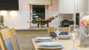 Een eetruimte met een lange houten tafel gedekt voor een maaltijd, een opgehangen stuk vlees en een raam met uitzicht op de stad.