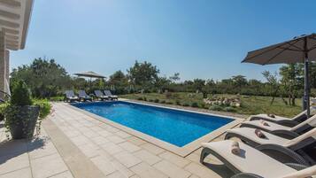 A rectangular swimming pool with lounge chairs and umbrellas on a tiled patio.