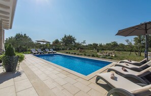 Piscina retangular com espreguiçadeiras e guarda-sóis em um terraço ladrilhado.