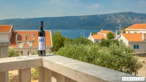 A balcony with a wine bottle and glasses, overlooking a coastal town with terracotta-roofed buildings and a view of the sea and mountains. - Nella Hvar in Rudina Hvar (Stari Grad)