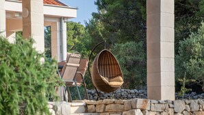 A pool area with stone steps leading to a lounge chair and a hanging chair, surrounded by greenery and a building with a tiled roof. - Nella Hvar in Rudina Hvar (Stari Grad)
