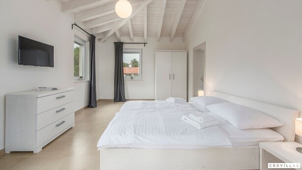 Een slaapkamer met een bed, een televisie, een kledingkast en een raam met gordijnen.