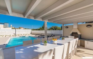 Une terrasse extérieure avec une piscine, un coin repas et un barbecue.
